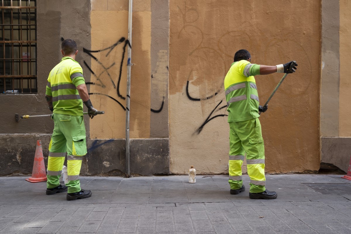 Dos treballadors del servei de neteja traient les pintades d'una paret - Ajuntament de Barcelona Dos treballadors del servei de neteja traient les pintades d'una paret - Ajuntament de Barcelona