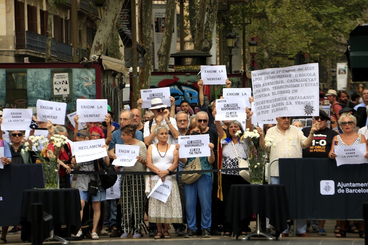 Persones amb cartells protestant a l'acte de commemoració dels cinc anys dels atemptats del 17 d'agost per la investigació que s'ha fet del 17-A, a la Rambla de Barcelona - ACN