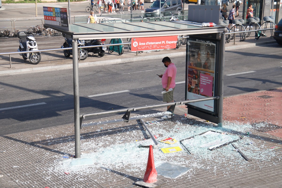 Marquesina d'autobus trencada i motos cremades al fons, a Plaça Espanya - ACN