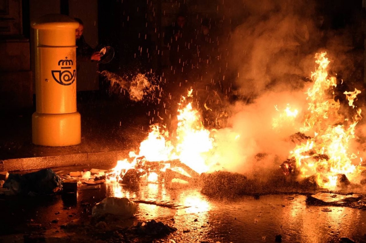 Un veï de Gràcia intentant apagar un foc que s'ha encès en la cinquena nit d'incidents a Barcelona  - Adrià Costa