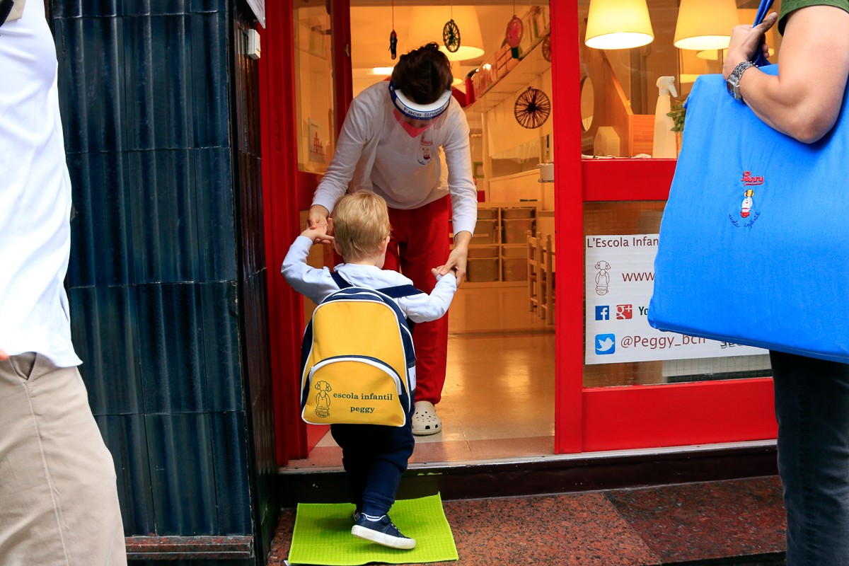 Un infant entra, acompanyat de la mestra, a l'escola infantil Peggy de Barcelona, després de trepitjar un drap amb desinfectant - Laura Fíguls/ACN