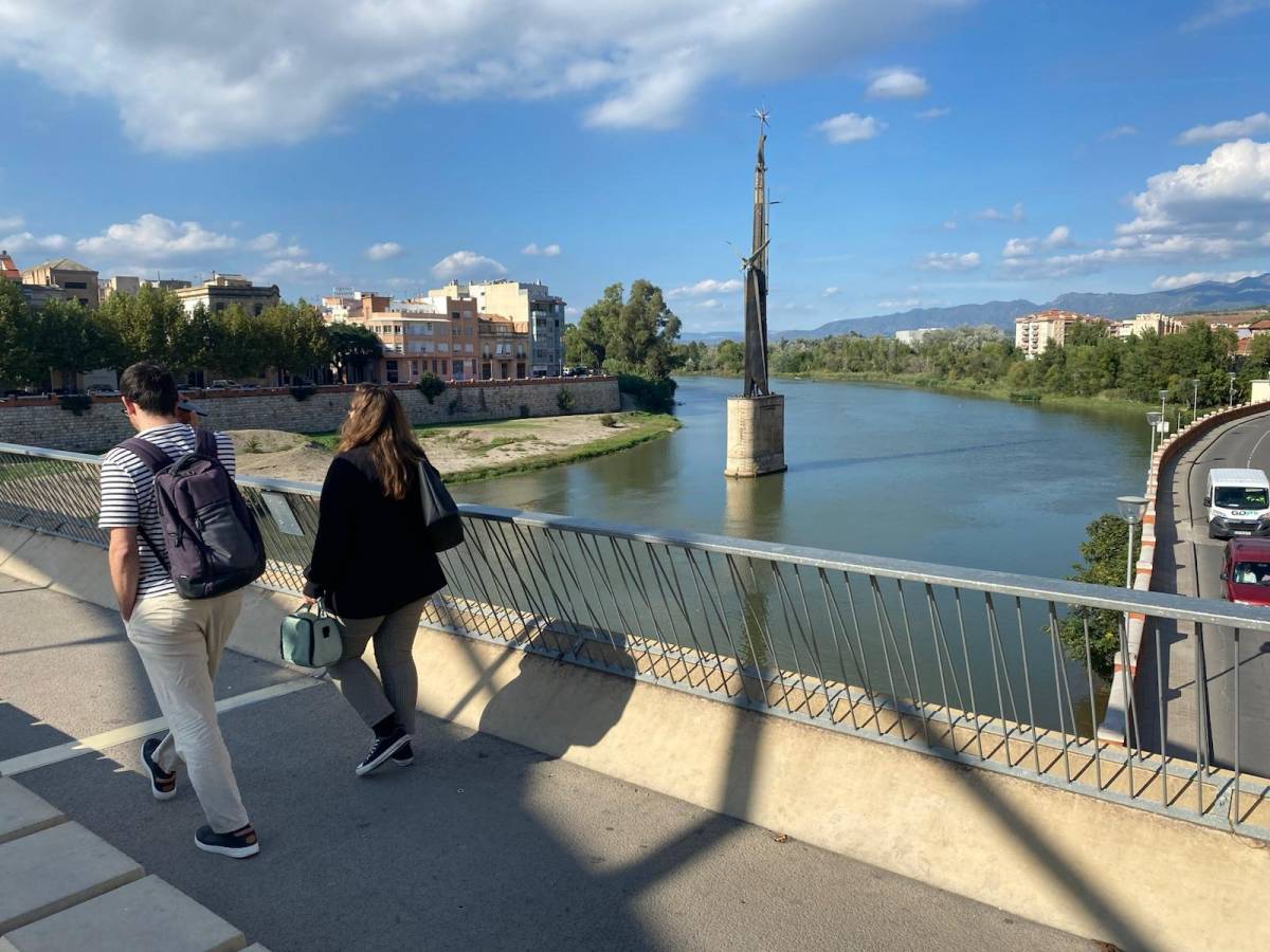 Dos vianants travessant el pont davant del monòlit franquista.