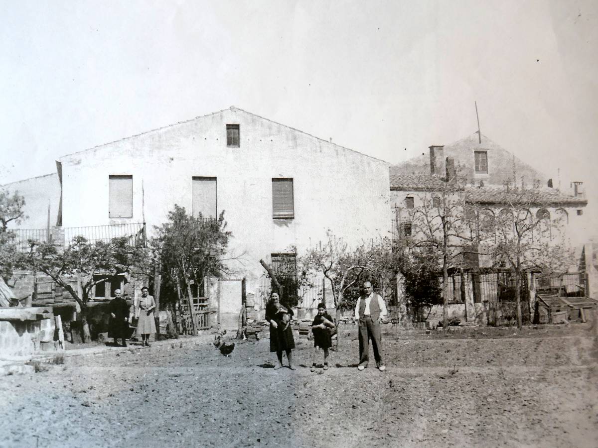 Mercè Elias entre el pare i la mare, amb la casa, l’hort i unes gallines en una foto antiga - Mercè Elias entre el pare i la mare, amb la casa, l’hort i unes gallines en una foto antiga